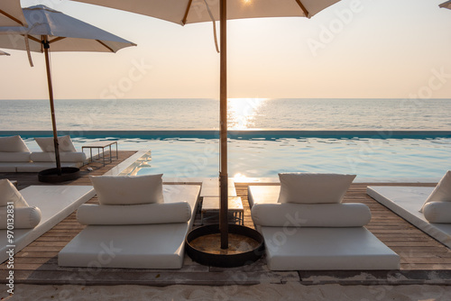 Fototapeta Naklejka Na Ścianę i Meble -  swimming pool on sea view and umbrella and chair in hotel resort with sunset
