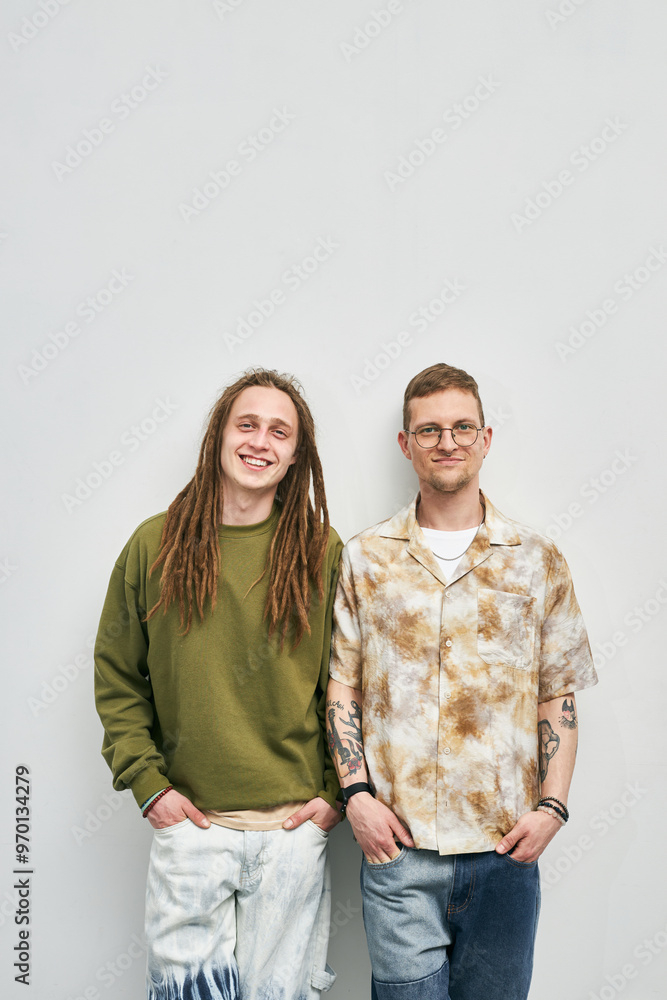 Two men standing together, one with dreadlocks and a green sweater and other with tattoos and glasses, displaying casual style and cheerful expressions Two men standing together, one with dreadlocks and a green sweater and other with tattoos and glasses, displaying casual style and cheerful expressions