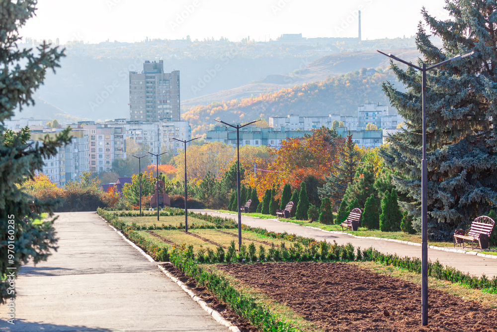 Central park in Rybnitsa town from Transnistria in Moldova. Serene park scene featuring a sidewalk and bench under a lush trees