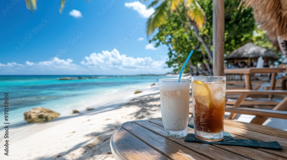 Two refreshing beverages, one with a straw, are placed on a wooden table by the beach, with a stunning blue ocean, lush palm trees, and a clear sky creating a perfect tropical setting. Two refreshing beverages, one with a straw, are placed on a wooden table by the beach, with a stunning blue ocean, lush palm trees, and a clear sky creating a perfect tropical setting.