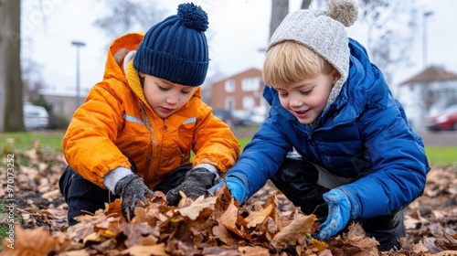 Two children, dressed in warm winter clothing, excitedly play with fallen autumn leaves outdoors, showcasing the joy of childhood and changing seasons. photo