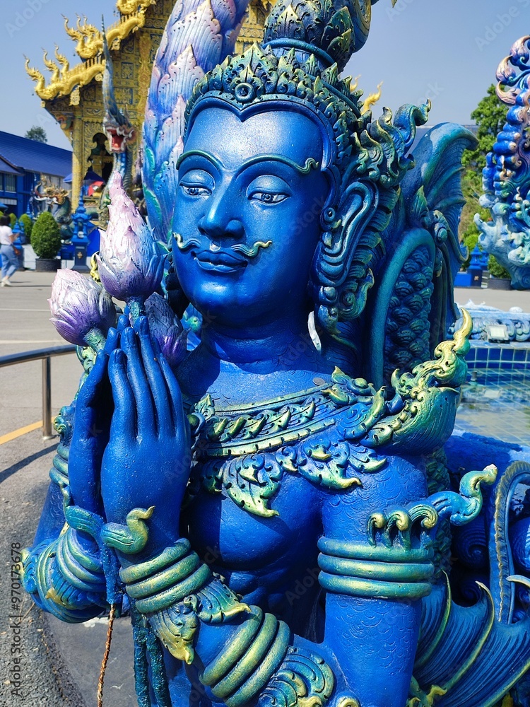 Fototapeta premium This vibrant close-up captures a blue deity sculpture at Wat Rong Suea Ten, the Blue Temple, in Chiang Rai, Thailand. The figure is adorned with intricate details and golden highlights.