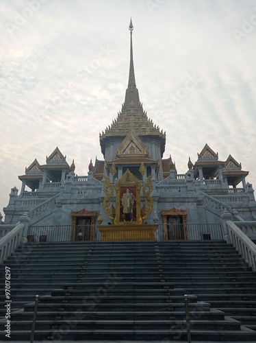 A majestic view of the steps leading up to the Golden Buddha Temple (Wat Traimit) in Bangkok, showcasing its grand spire and intricate architectural details under a serene sky.

 photo