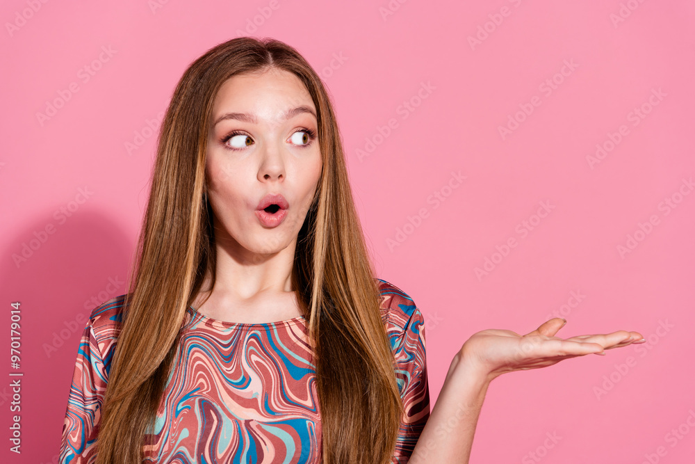 Photo of astonished girl with straight hairdo wear print t-shirt look at object on palm empty space isolated on pink color background Photo of astonished girl with straight hairdo wear print t-shirt look at object on palm empty space isolated on pink color background