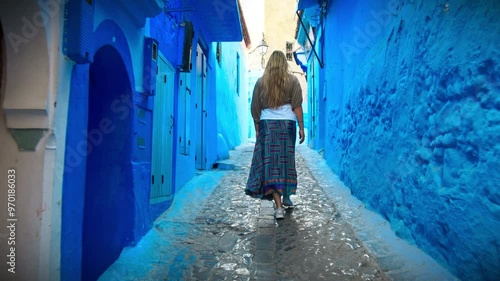 European blonde girl walking in Medina alleys and stairs of Chefchaouen, the famous Blue Pearl of Morocco or Blue City. Chaouen is noted for its buildings in shades of blue, UNESCO heritage.