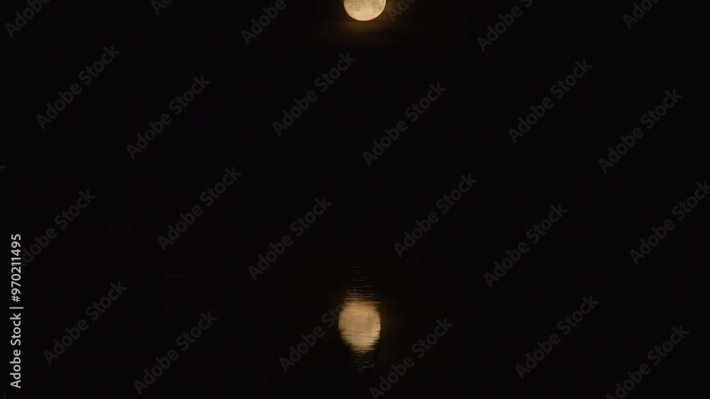 The orange moon at night is reflected in the rippling water The orange moon at night is reflected in the rippling water