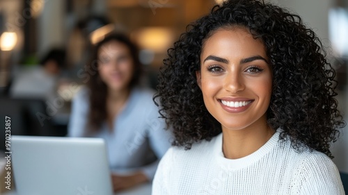 A woman with curly hair is smiling and sitting in front of a laptop