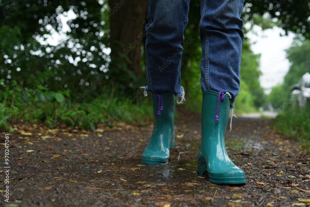 Woman in turquoise rubber boots walking on wet road, closeup. Space for text Woman in turquoise rubber boots walking on wet road, closeup. Space for text