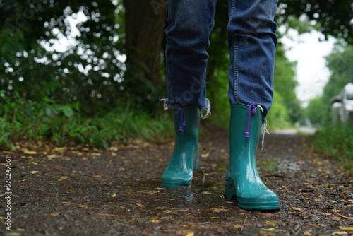 Woman in turquoise rubber boots walking on wet road, closeup. Space for text