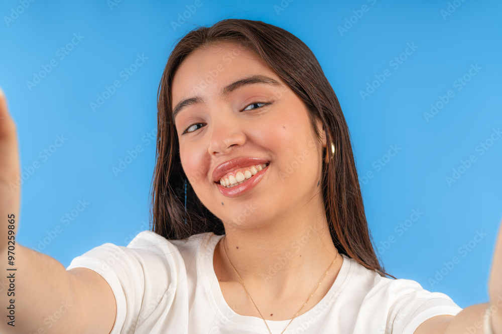 Young woman taking a selfie and smiling with blue background Young woman taking a selfie and smiling with blue background