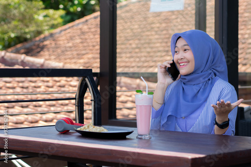 young Asian woman in hijab making a phone call while relaxing at a cafe. photo