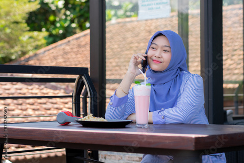 young Asian woman in hijab making a phone call while relaxing at a cafe. photo