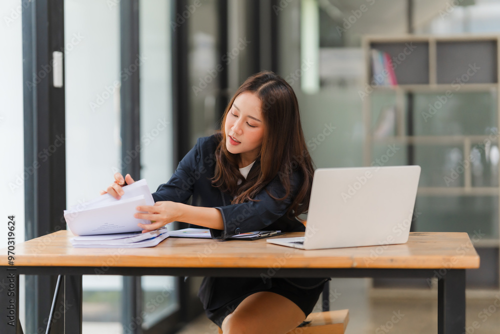 Focused and Determined: A young businesswoman, dressed in a professional blazer, meticulously reviews documents at her desk, showcasing dedication and focus in a contemporary office setting. Focused and Determined: A young businesswoman, dressed in a professional blazer, meticulously reviews documents at her desk, showcasing dedication and focus in a contemporary office setting.