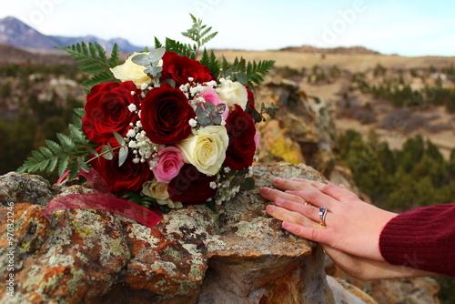 Newly weds interlace hands next to wedding bouquet in mountain landscape 