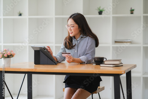 Seamless Online Shopping: Young Asian Woman Using Credit Card and Tablet - A young Asian woman experiences the ease of online shopping, effortlessly making a purchase on her tablet with a credit card.