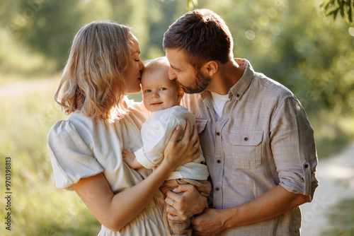 Wallpaper Mural A family of three, a man and a woman with a child in their arms, stand in a park in the summer. The concept of a happy family with a small child, care and love. Torontodigital.ca