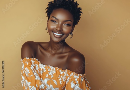 Smiling woman with short curly hair wearing an orange floral top against a wa...