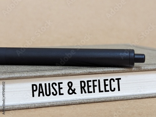 a book and black pen with the words Pause & Reflect