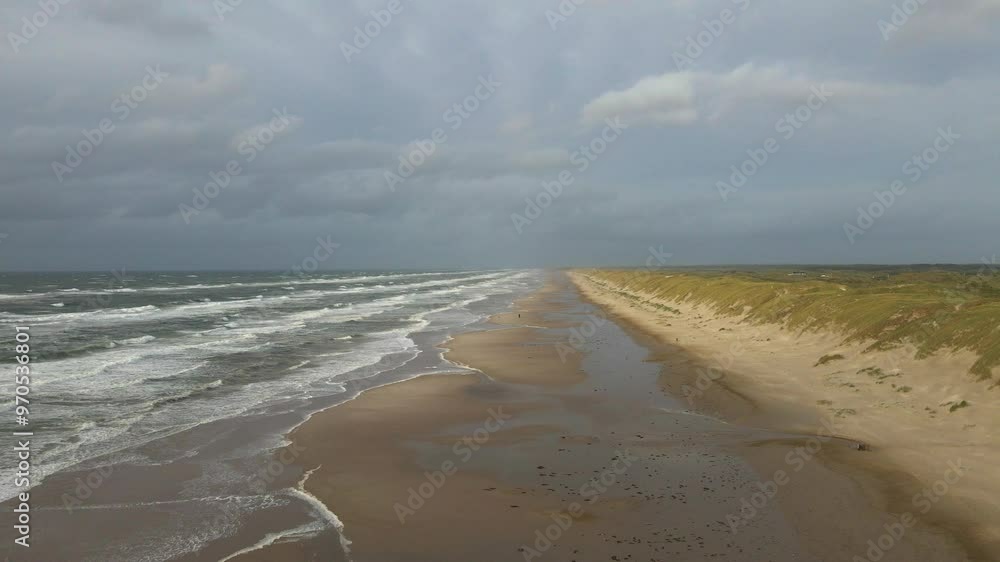 a drone flies at high altitude along the hvide sande beach, capturing wide views of the stormy danish coastline, gray skies, and turbulent sea under a moody evening sky with the dunes to the right a drone flies at high altitude along the hvide sande beach, capturing wide views of the stormy danish coastline, gray skies, and turbulent sea under a moody evening sky with the dunes to the right