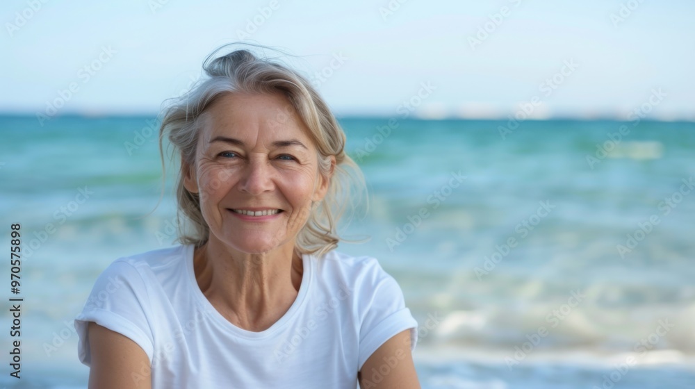 smiling attractive older woman in white t - shirt sitting against the background of the sea