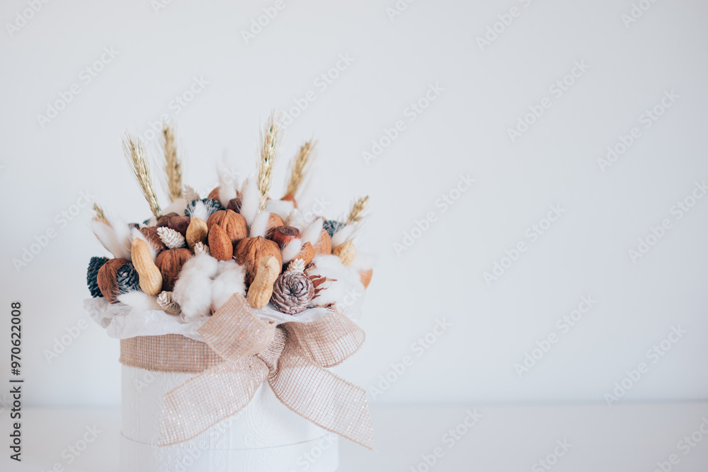 Obraz premium Beautiful handmade Christmas bouquet of nuts, pinecones and cotton flowers in round gift box against white background. Holiday floral decor. Copy space for text.