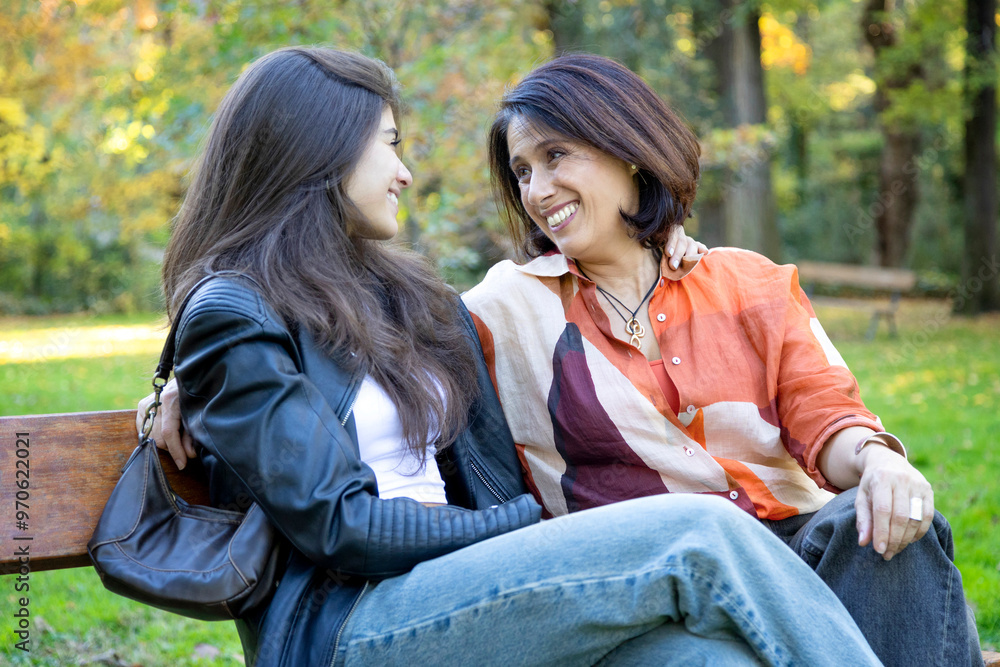 Mother and daughter sharing a warm smile while relaxing on a park bench. Mother and daughter sharing a warm smile while relaxing on a park bench.