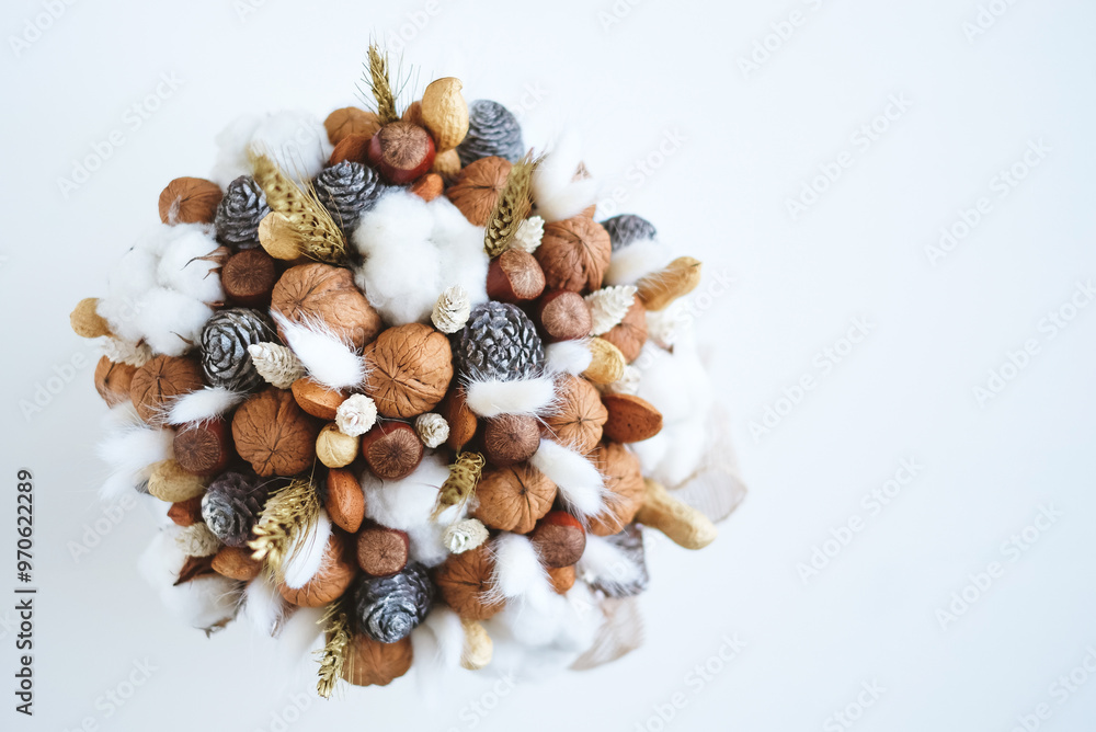 Obraz premium Beautiful handmade Christmas bouquet of nuts, pinecones and cotton flowers, top down view on white background. Holiday floral decor. Copy space for text.