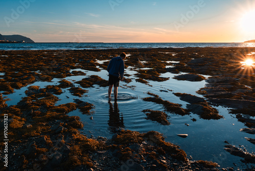 Teen exploring tidal pools on rocky beach in Newfoundland at sunset.