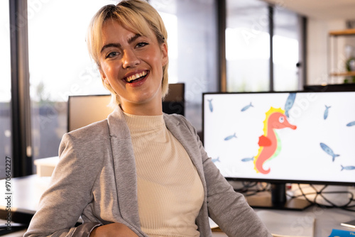 Smiling woman in office with computer displaying seahorse and fish illustration photo