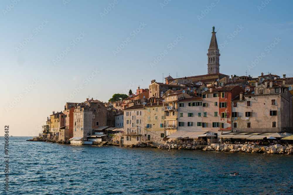 Fototapeta premium As the sun sets over Rovinj, Croatia, the vibrant colors of the waterfront buildings reflect in the calm waters, creating a picturesque view full of charm and history