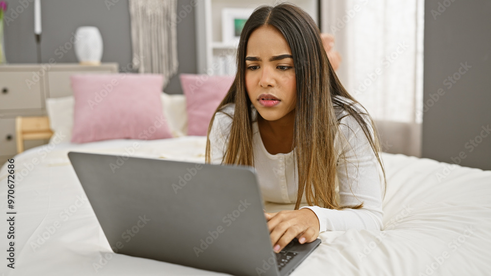 Focused hispanic woman using laptop in a cozy bedroom setting, portraying modern indoor lifestyle and technology use. Focused hispanic woman using laptop in a cozy bedroom setting, portraying modern indoor lifestyle and technology use.