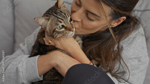 Photography A young hispanic woman cuddles and kisses her pet cat in the living room, displaying affection and warmth while indoors with her feline companion