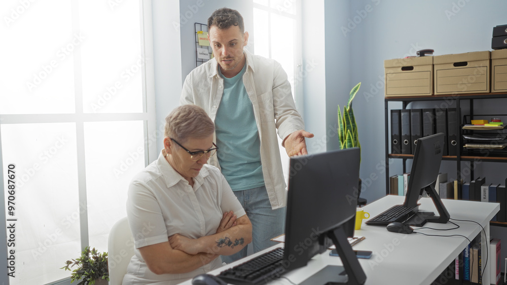 Woman and man working indoors in an office discussing business with computers in a modern workplace setting Woman and man working indoors in an office discussing business with computers in a modern workplace setting