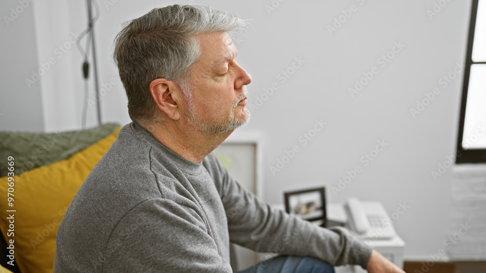 Obraz premium Serene mature man with grey hair in a casual setting at home, embodying tranquility and contemplation.