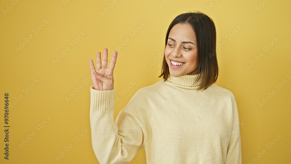 Smiling young woman making number three gesture against a yellow background in a cream sweater Smiling young woman making number three gesture against a yellow background in a cream sweater