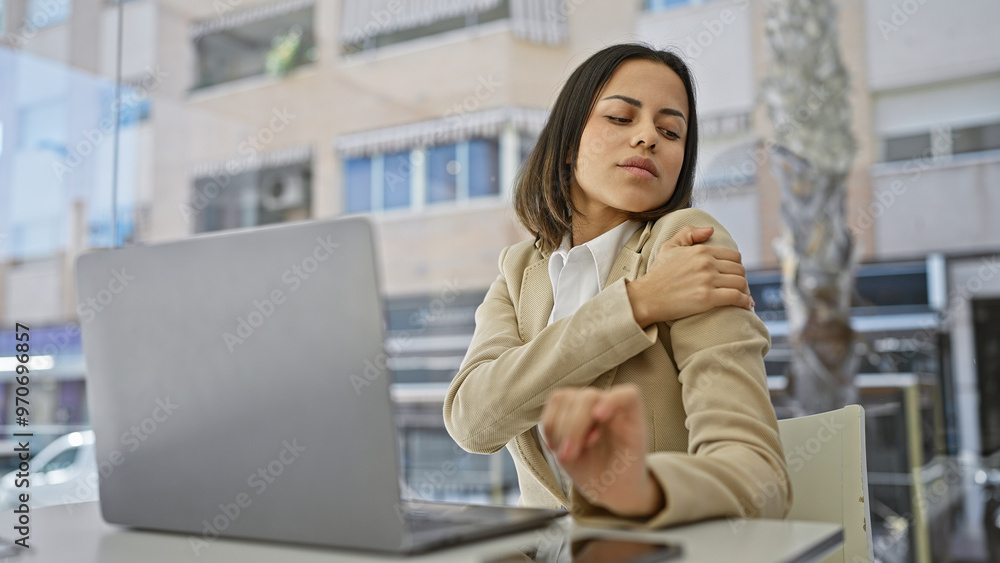 A hispanic woman in businesswear expressing discomfort or pain while working on her laptop outdoors. A hispanic woman in businesswear expressing discomfort or pain while working on her laptop outdoors.