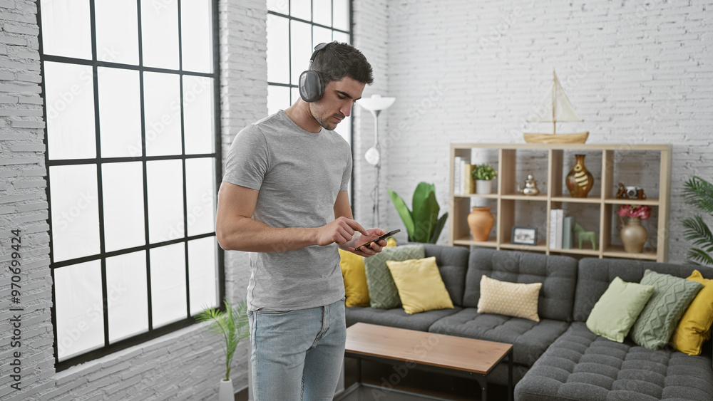 Handsome young man with headphones using smartphone in modern living room. Handsome young man with headphones using smartphone in modern living room.