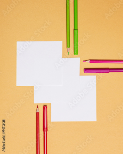 three square sheets of paper with pens and pencils on orange background