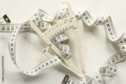 Plastic body fat caliper and measuring tape on white table, top view