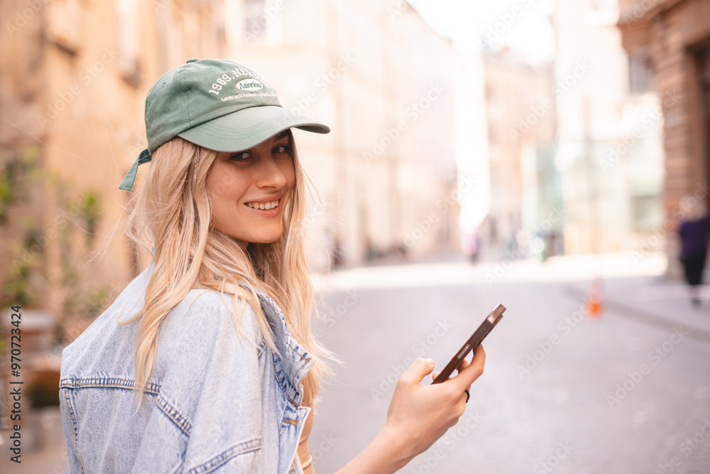 Beautiful smiling woman walking on street chatting on mobile phone. Girl talking on smartphone, texting, sending message, green cap and jeans jacket. Girl turn her head. Beautiful smiling woman walking on street chatting on mobile phone. Girl talking on smartphone, texting, sending message, green cap and jeans jacket. Girl turn her head.