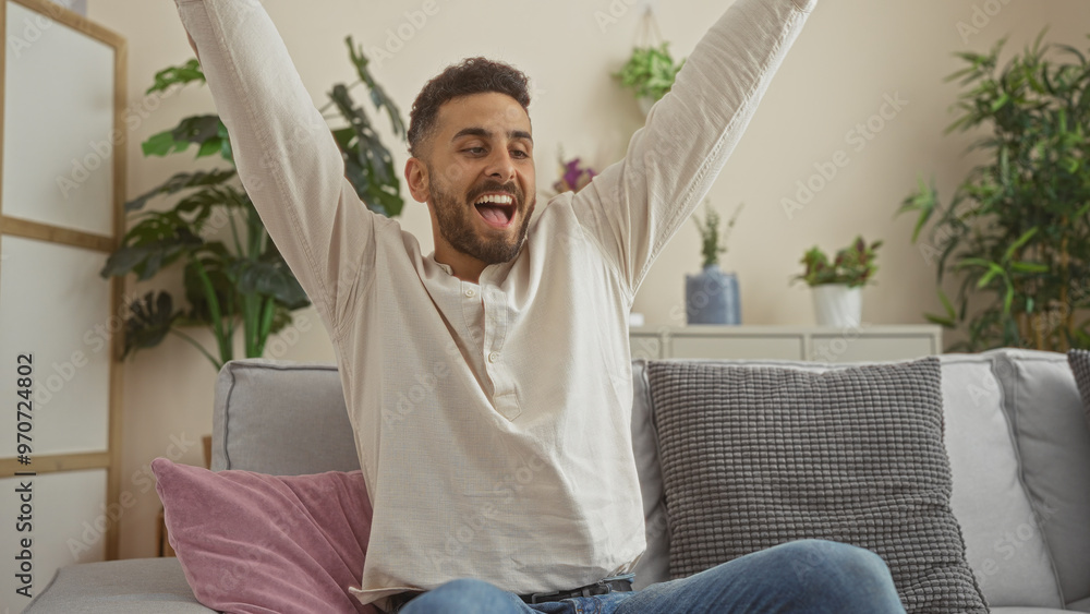 Handsome young hispanic man indoors at home looking happy and relaxed in a well-decorated living room. Handsome young hispanic man indoors at home looking happy and relaxed in a well-decorated living room.