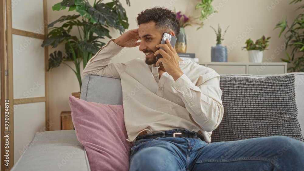 A young hispanic man having a phone conversation while relaxing on a comfortable sofa in his stylishly decorated living room apartment, surrounded by plants and cozy pillows. A young hispanic man having a phone conversation while relaxing on a comfortable sofa in his stylishly decorated living room apartment, surrounded by plants and cozy pillows.