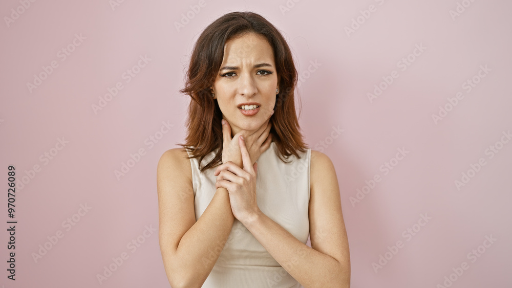 Young hispanic woman with a sore throat isolated against a pink wall, looking uncomfortable and touching her neck. Young hispanic woman with a sore throat isolated against a pink wall, looking uncomfortable and touching her neck.