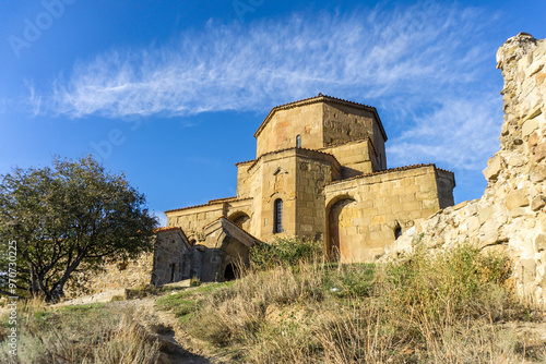 Jvari Monastery close view. Ruins of the tower and fortress wall. Green grass, bright blue sky photo