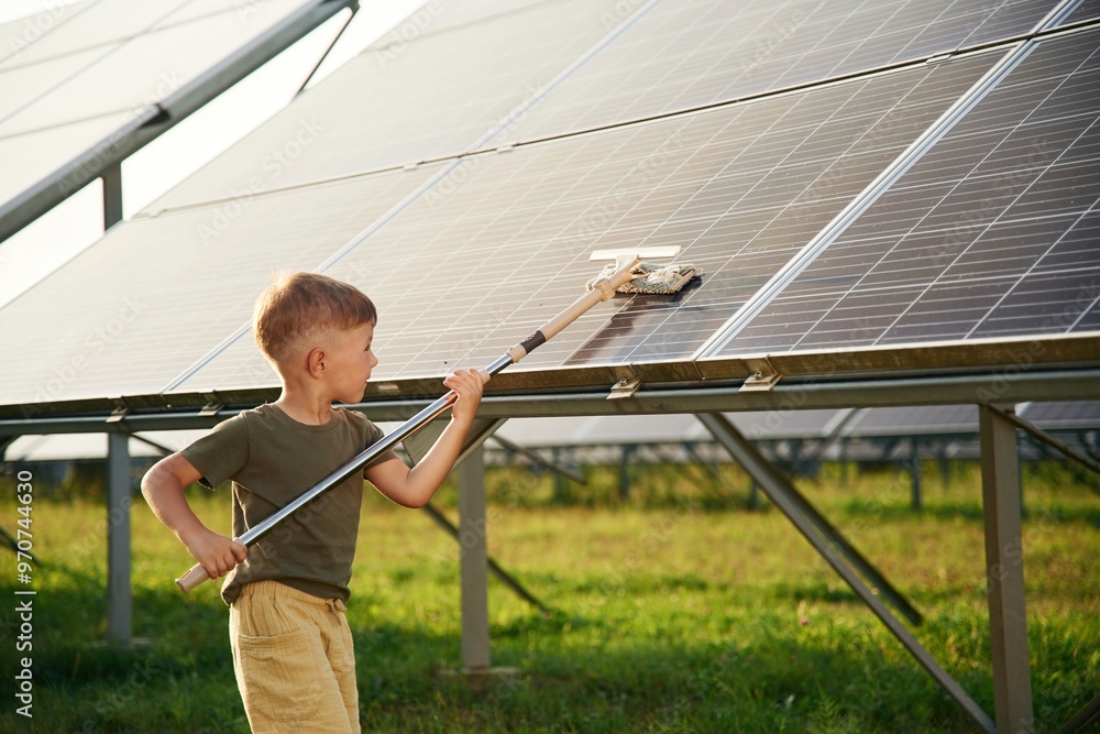 Busy by cleaning the surface. Little boy is with solar panels outdoors Busy by cleaning the surface. Little boy is with solar panels outdoors