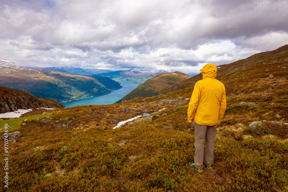 Tourist looks at the panoramic view of Innvikfjord from Mount Hoven. Beautiful mountain landscape. Stryn Municipality, Loen, Norway Tourist looks at the panoramic view of Innvikfjord from Mount Hoven. Beautiful mountain landscape. Stryn Municipality, Loen, Norway