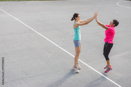 Two women jogging together on an outdoor track, smiling and enjoying their exercise. The background features green hills and trees, creating a serene atmosphere.