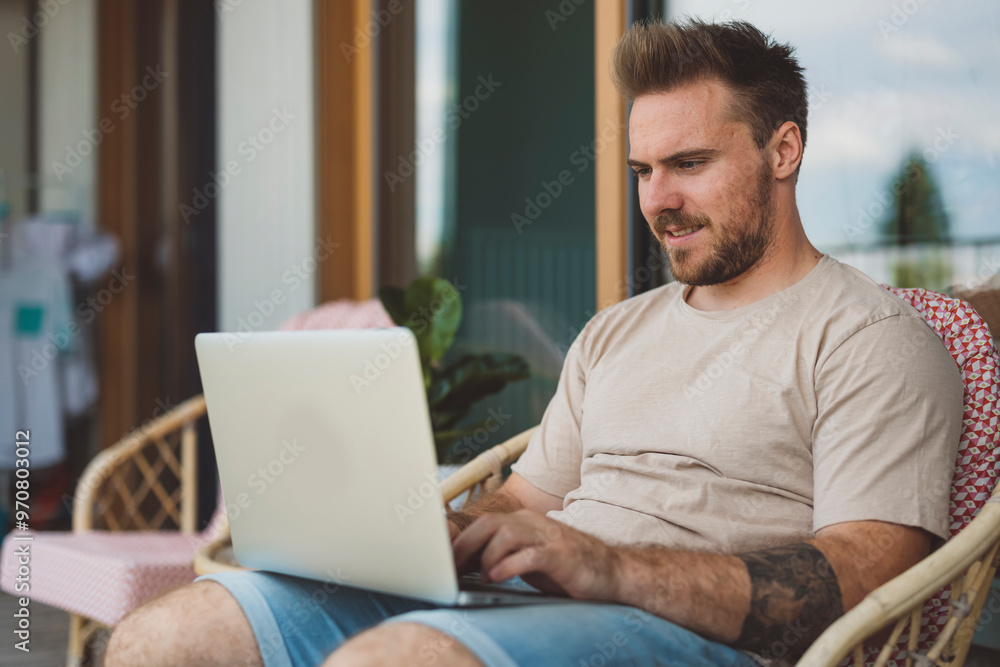 A man sitting outdoors, engaged in a phone conversation while working on a laptop. He appears focused and relaxed, with a casual outfit and a modern hairstyle. A man sitting outdoors, engaged in a phone conversation while working on a laptop. He appears focused and relaxed, with a casual outfit and a modern hairstyle.