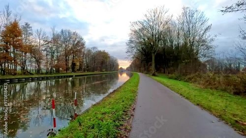 A serene and tranquil autumn scene showcasing a picturesque pathway that runs alongside a calm canal under a cloudy sky photo