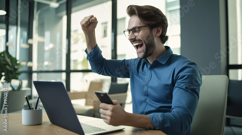 A happy man sitting at his desk raising his hands in celebration.